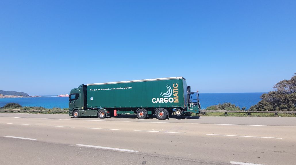 Camion de transport routier Cargomatic équipé d’un chariot embarqué lors de livraisons directes domicile et chantier en Corse, vue mer Méditerranée